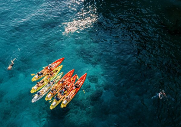 Tourists swim in the turquoise sea near a team of kayakers in kayaks. Drone